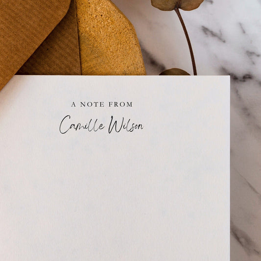 White notepad personalized with 'A Note from Camille Wilson' text on a marble surface with a brown envelope.