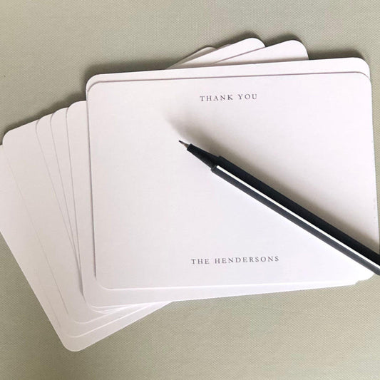 Stack of personalized thank you cards with a pen on a light gray surface