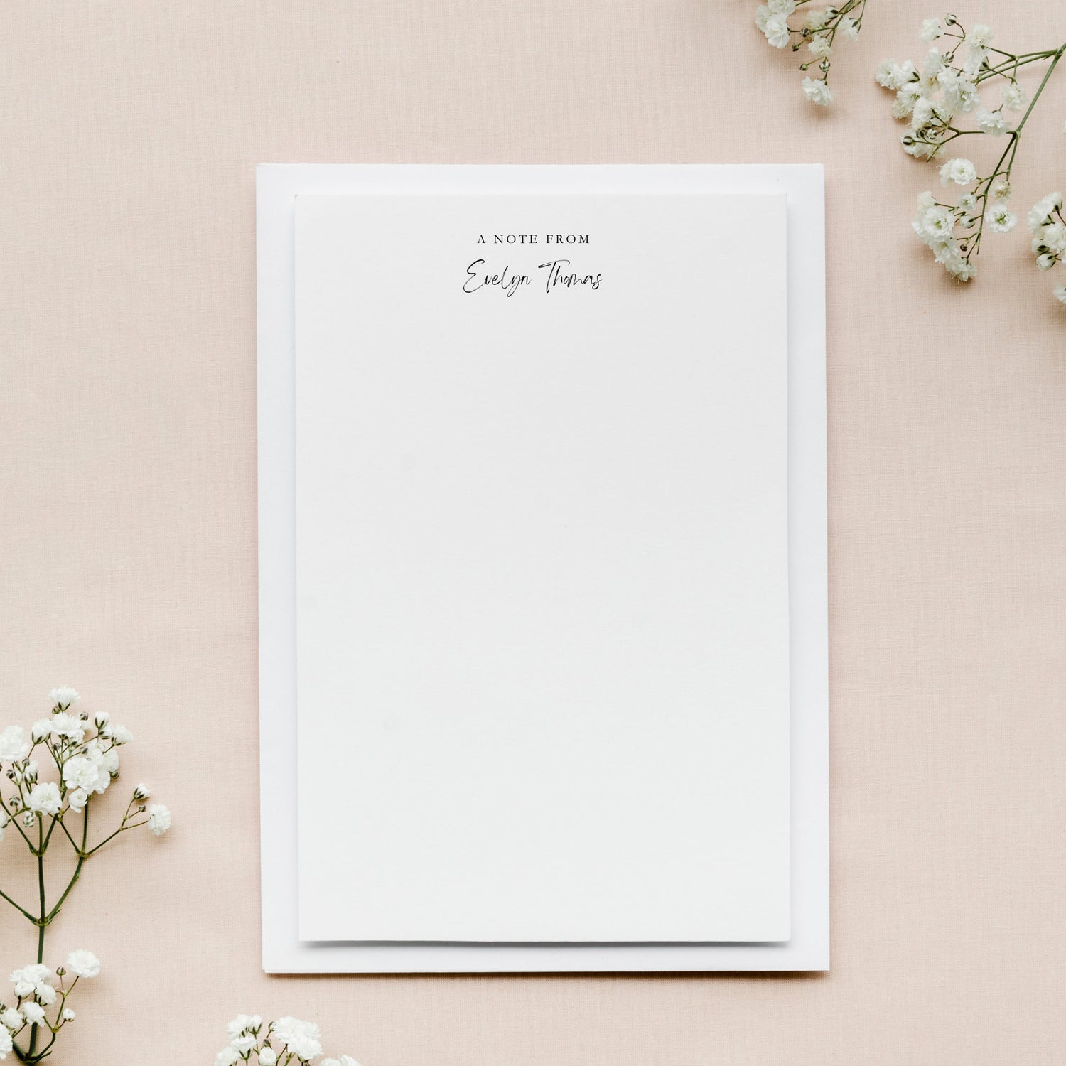 White notepad personalized with 'A Note from' text on a beige background with white flowers.