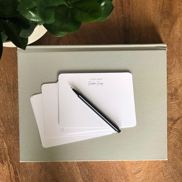 Set of white note cards with a pen on a light green box on a wooden surface.