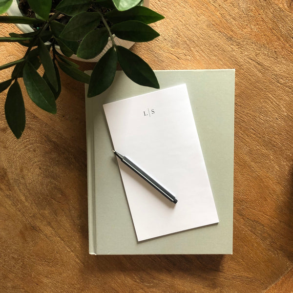 Notepad personalized with mongogram with a pen on a wooden surface next to a plant